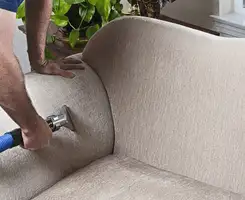 Professional upholstery cleaner deep-cleaning a fabric sofa with a handheld extraction tool and hose in Lakeland, FL.